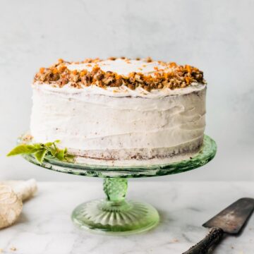 A two tiered round cake with white cream cheese frosting on a green cake stand.