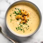 Bowl of roasted cauliflower soup topped with roasted cauliflower florets and parsley.