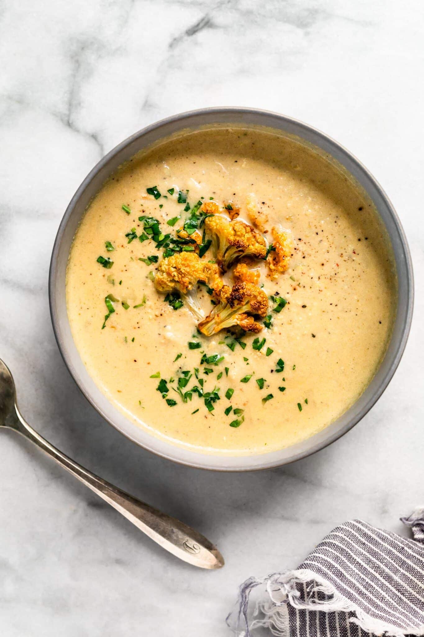 Bowl of roasted cauliflower soup topped with roasted cauliflower florets and parsley.