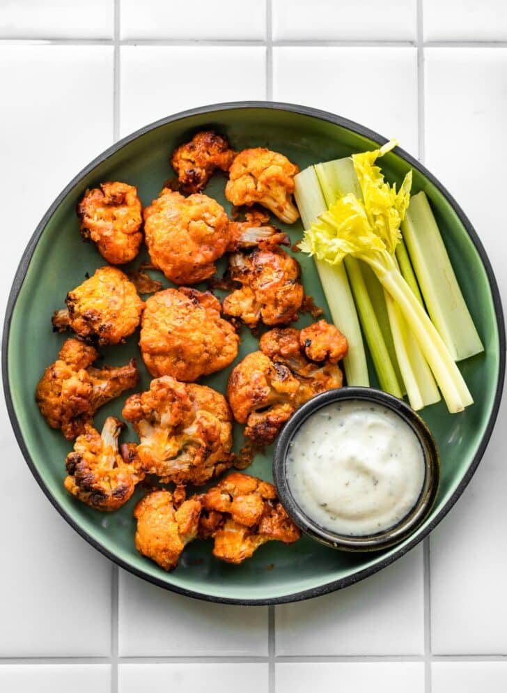 Overhead photo of vegan buffalo cauliflower in a green serving dish with celery and dip.