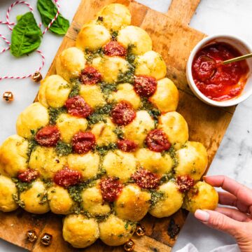 A woman's hand pulling a pizza dough ball from a gluten free Christmas tree.