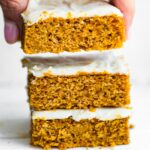 stack of frosted gluten free pumpkin bars with woman's hand grabbing the top bar