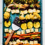 Overhead photo of baked Mediterranean vegetables on a sheet pan with a spatula.