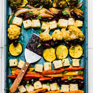 Overhead photo of baked Mediterranean vegetables on a sheet pan with a spatula.