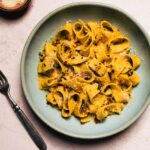 gluten-free pumpkin pasta with crispy bacon and parmesan served in a blue bowl with a fork on the side