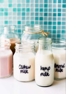 small glass bottles and mason jars filled with cashew milk, hemp milk, and almond milk