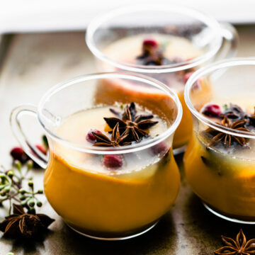 Three glasses filled with hot toddy, fresh fruit and spices floating in drink.