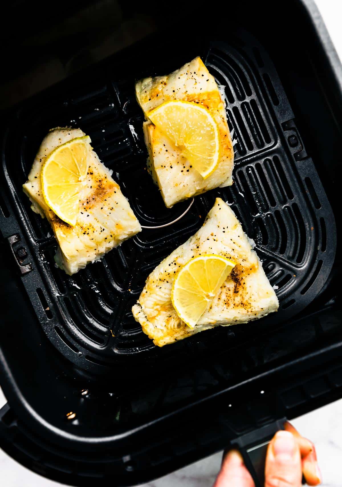 Three cooked fish filets topped with lemon in an air fryer