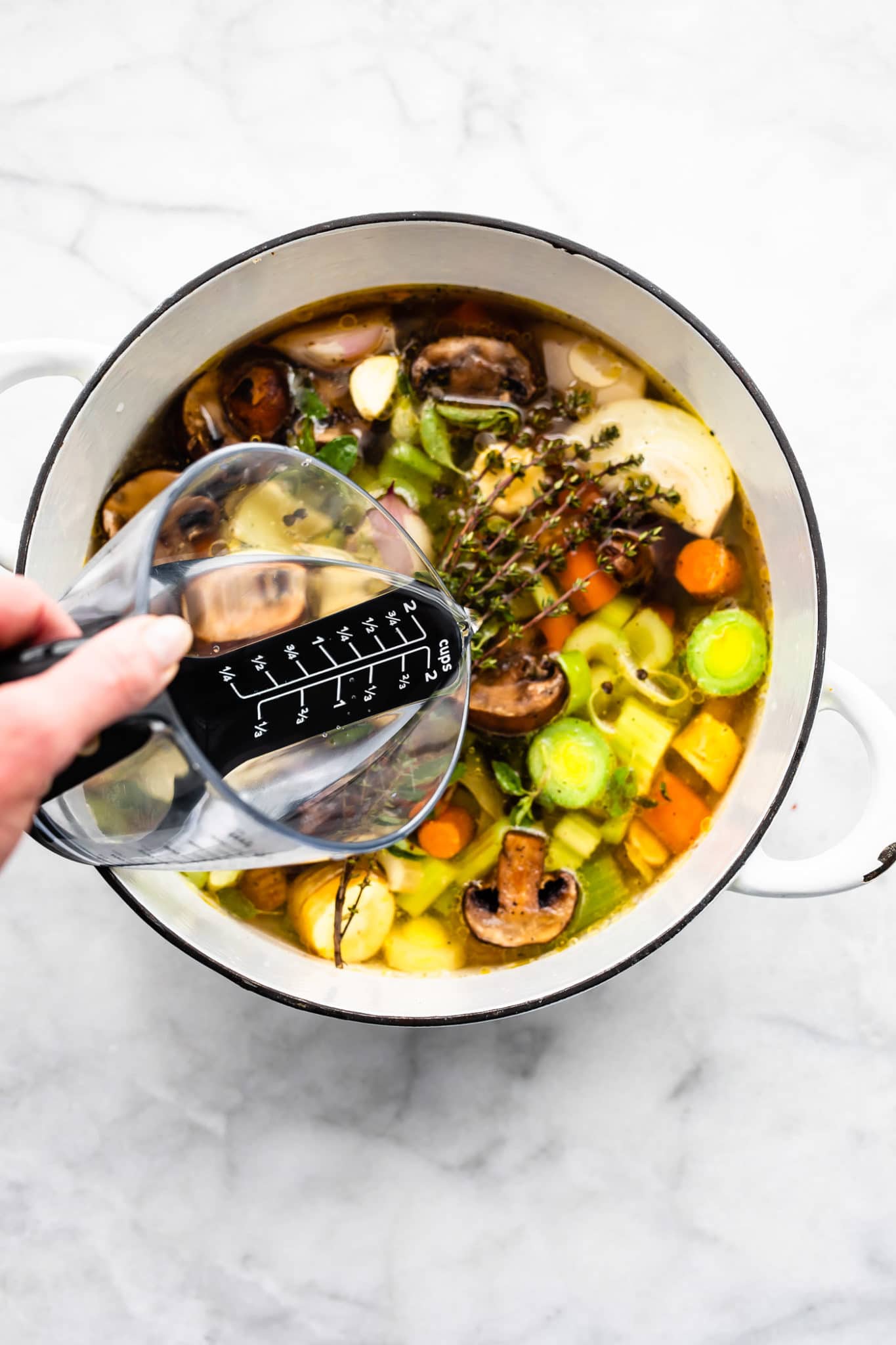 a woman's hand pouring water over a pot of vegetables showing how to make vegetable broth.