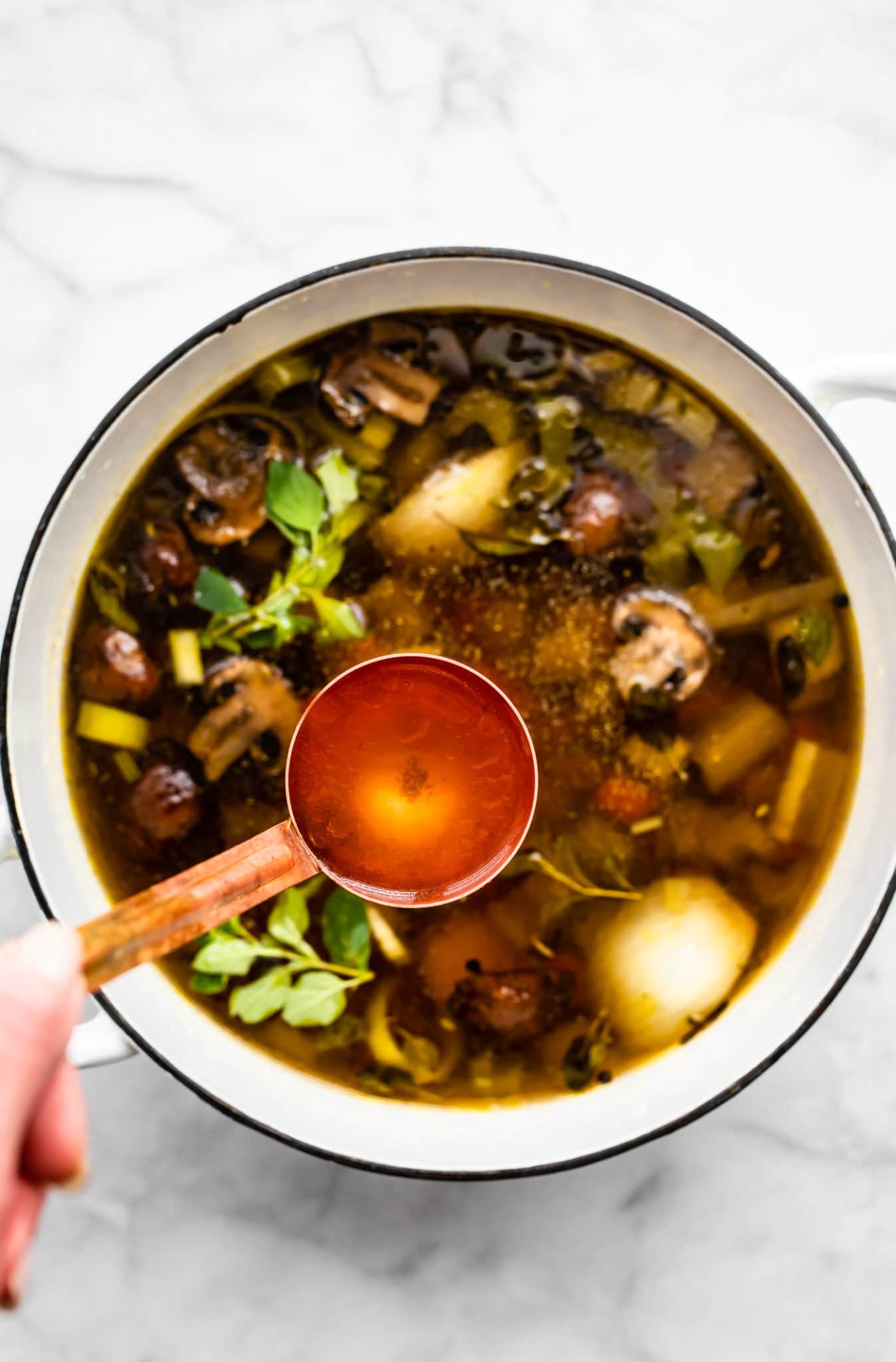 a tablespoon scooping out clear broth from a dutch oven filled with veggies to make homemade vegetable broth.