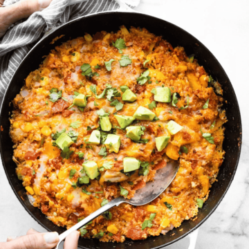 overhead image of one skillet mexican quinoa skillet toped with avocado with a hand dipping a spoon in the cneter