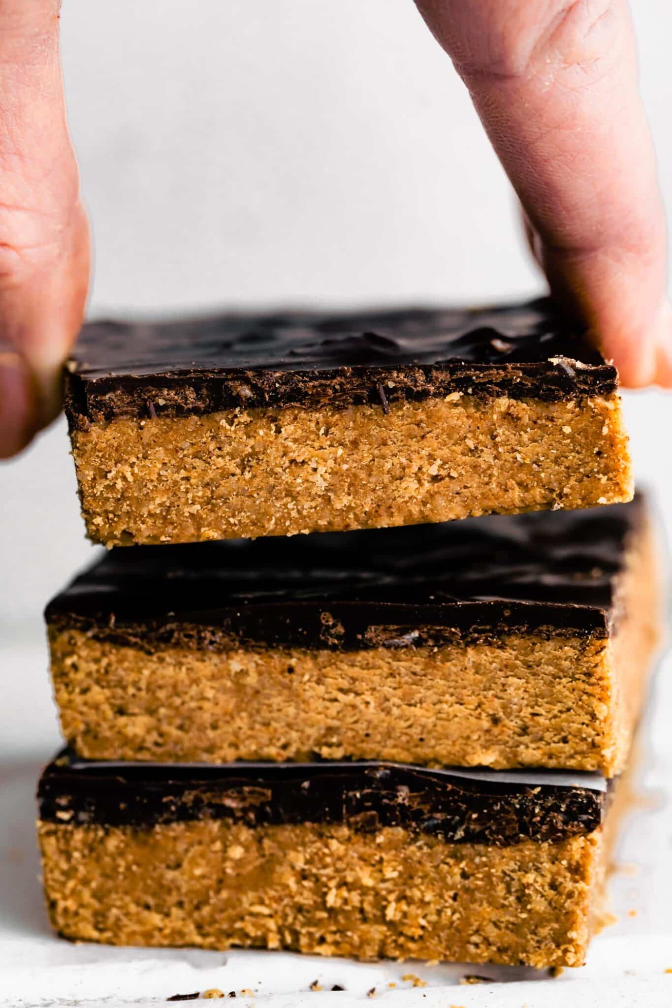 A woman's fingers lifting a no bake chocolate almond flour protein bar from the stack.