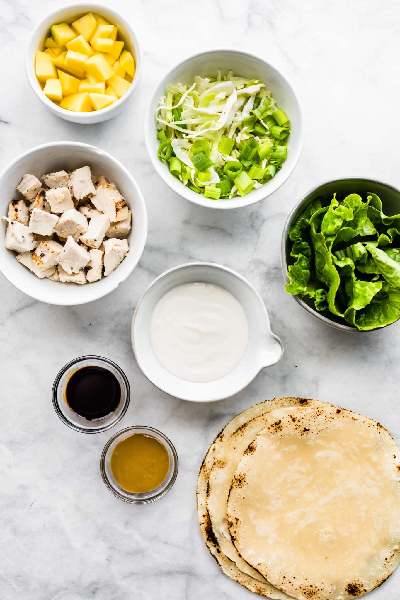 Ingredients for Asian chicken salad wraps on a white marble countertop.