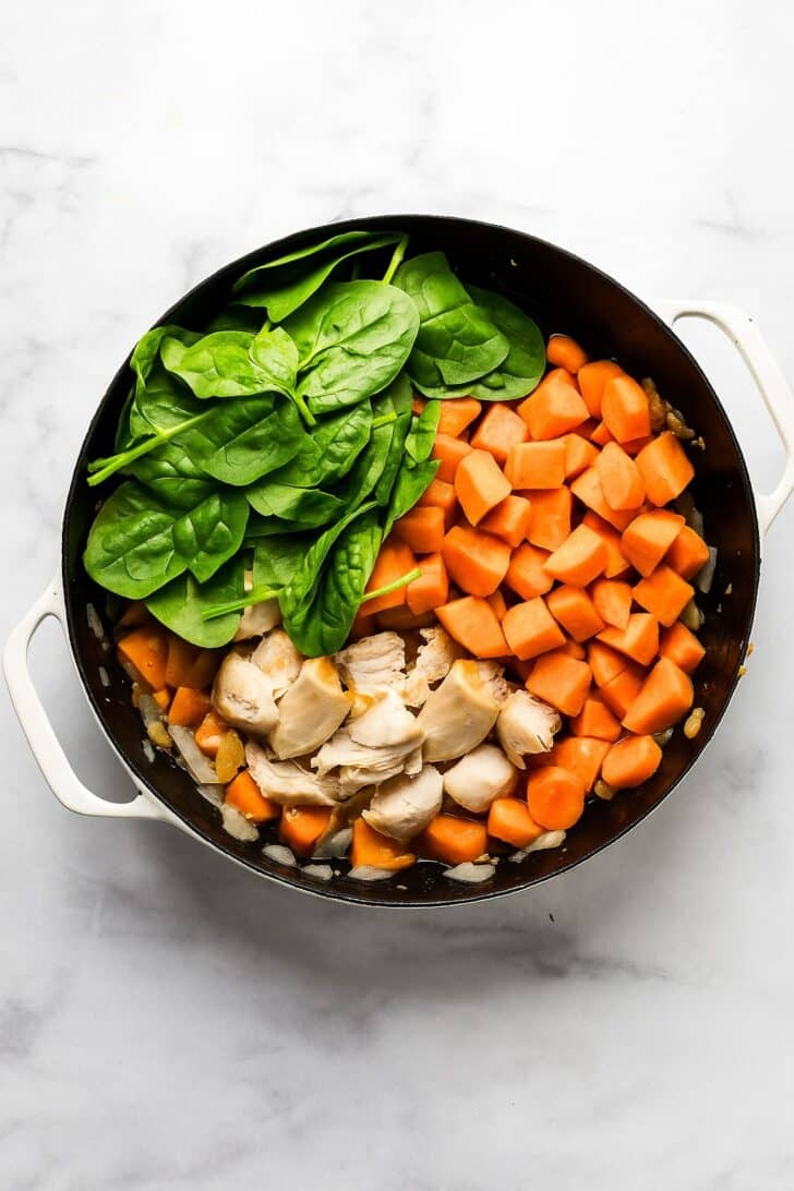 chopped sweet potato, carrot, spinach, nion and browned chicken in a black skillet