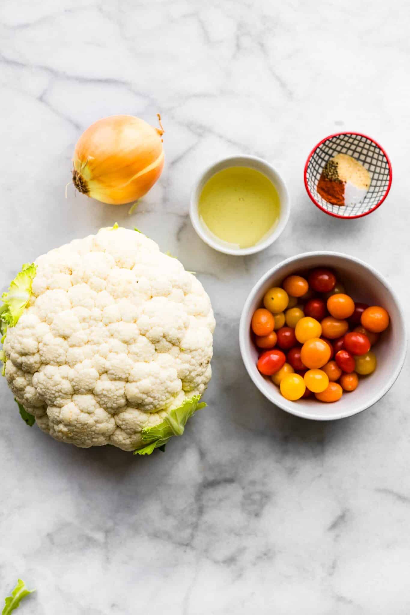 Ingredients to make cauliflower steaks including cherry tomatoes, onion, oil, and spices.