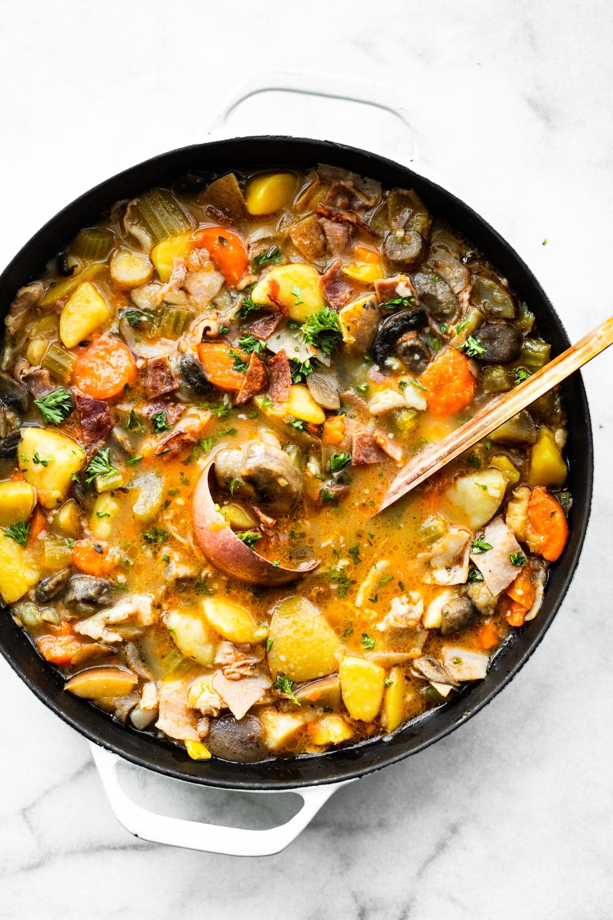 Pot full of slow cooker vegetable soup with bacon with copper ladle full of soup.
