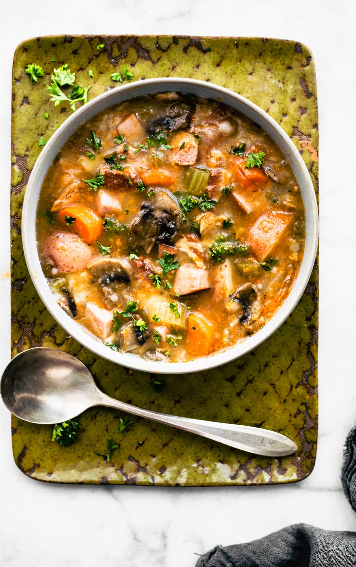 Bowl of slow cooker vegetable soup with bacon topped with parsley on a green tray.