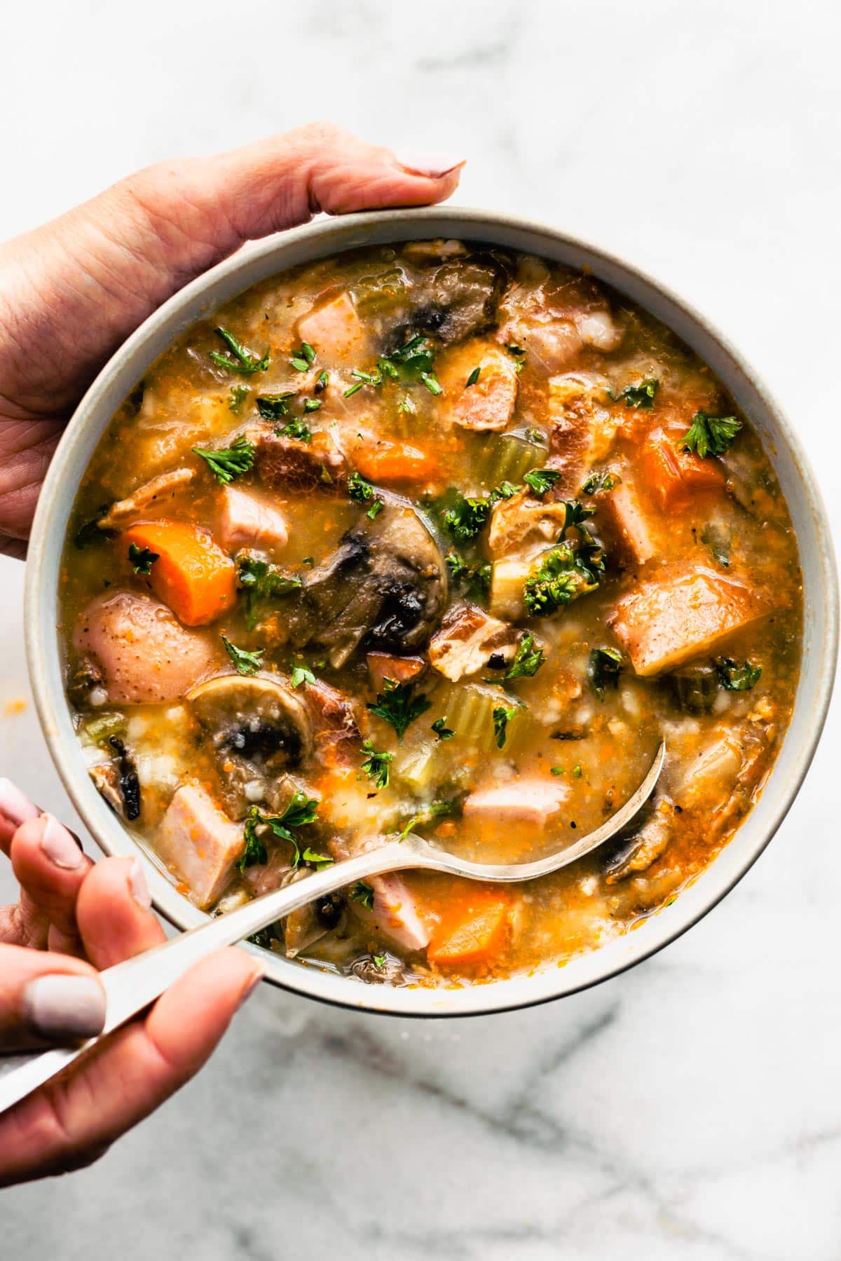Spoon dipping into a bowl full of slow cooker vegetable soup with bacon.