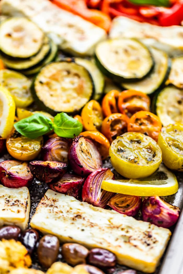 Greek roasted vegetables with a block of feta on a sheet pan. close up photo.