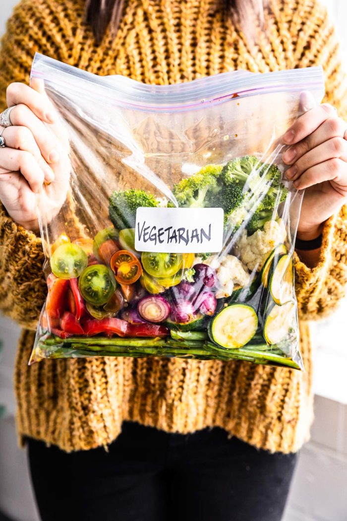 A woman holding a bag of vegetables in a marinade labeled "vegetarian".