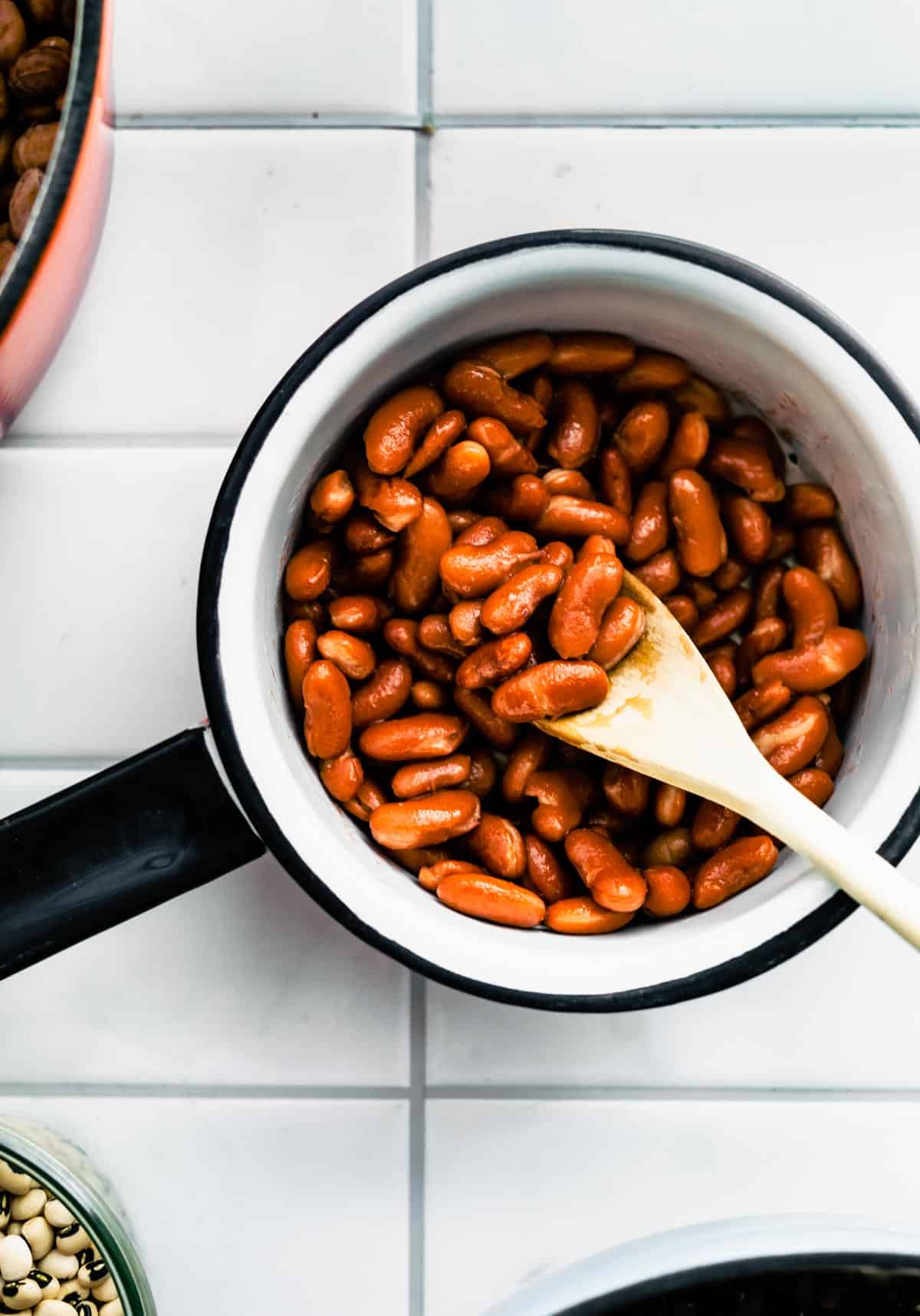 Overhead shot of a wooden spoon picking up cooked red Kidney Beans from a pot.