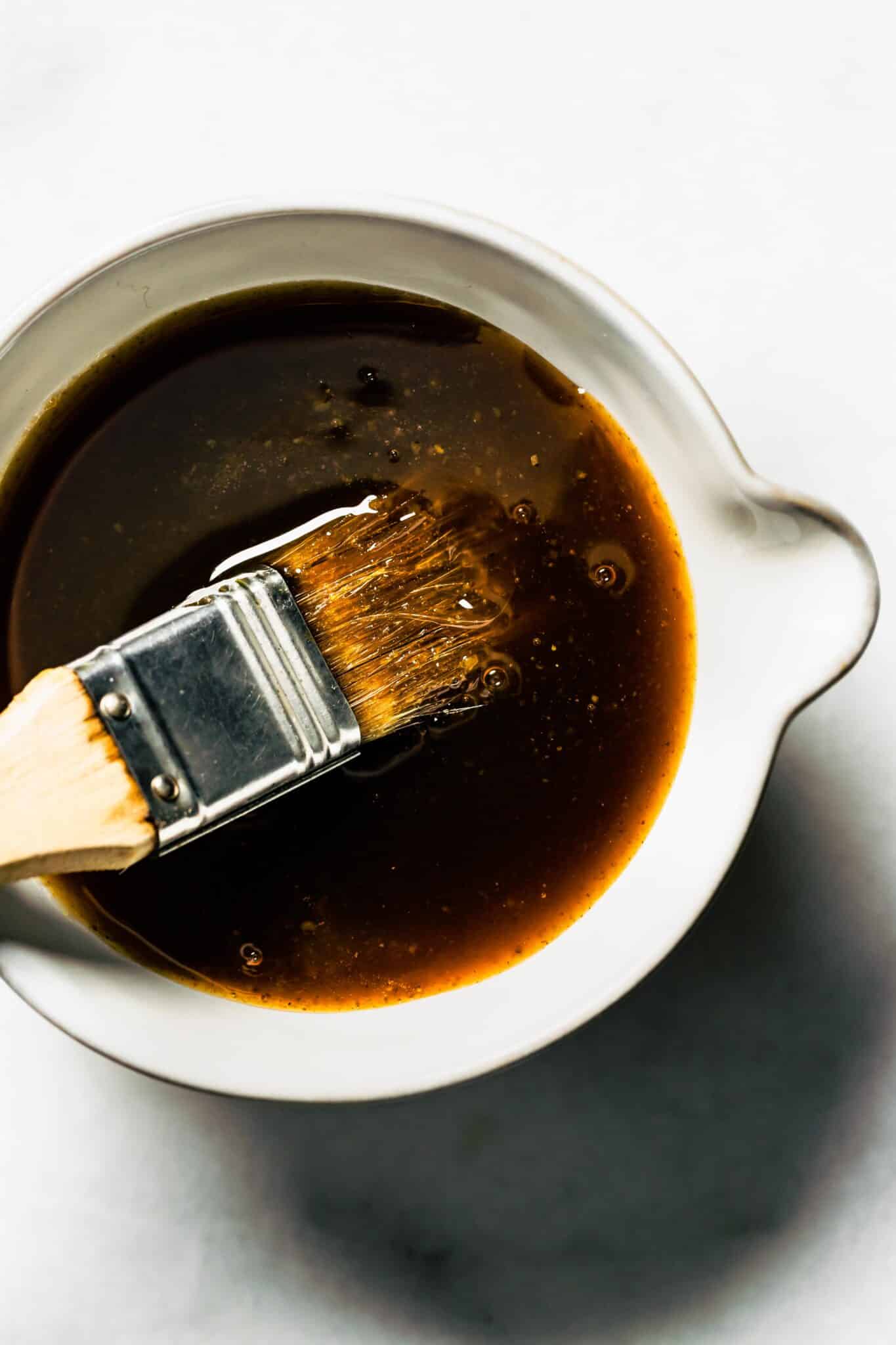 Up close photo of maple bourbon glaze in a white dish with a brush.