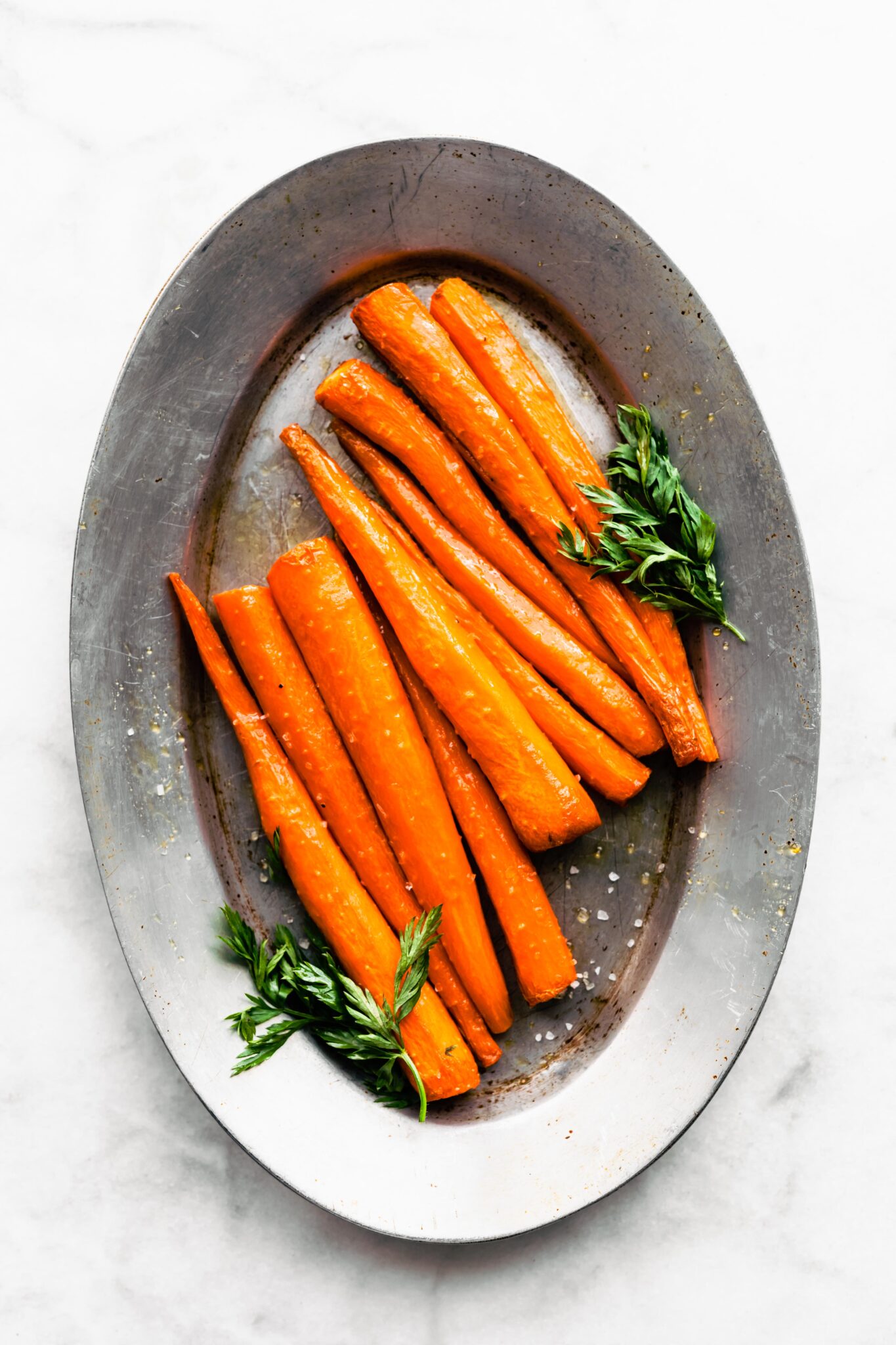 Overhead photo of saucy maple glazed carrots sprinkled with flaked sea salt.