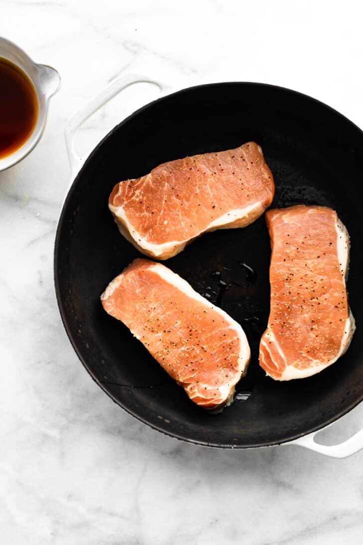Three boneless pork chops seasoned with salt and pepper in a cast iron skillet.