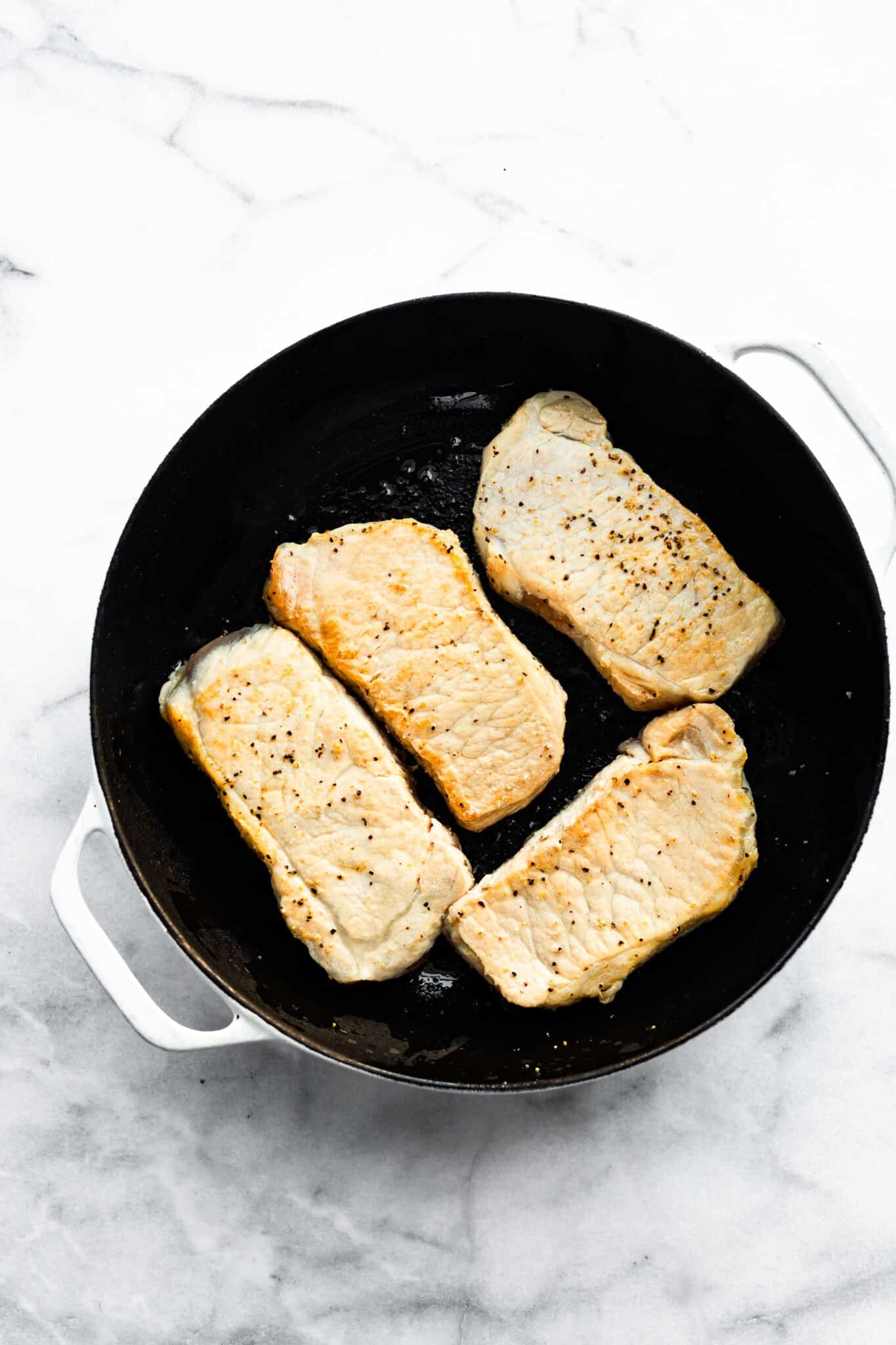 Four cooked boneless pork chops in a cast iron skillet.