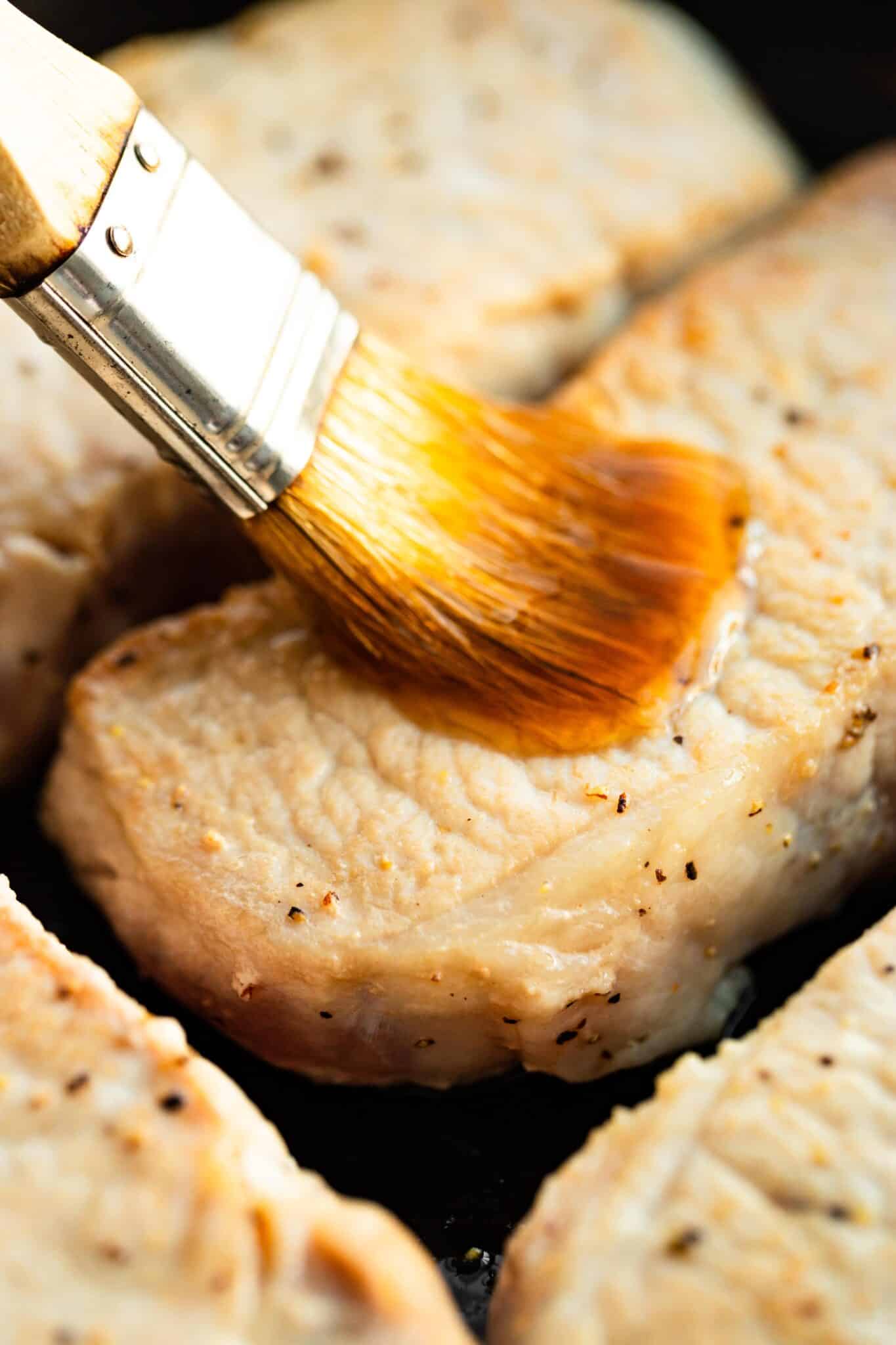 Brushing on maple bourbon glaze onto a seared pork chop.