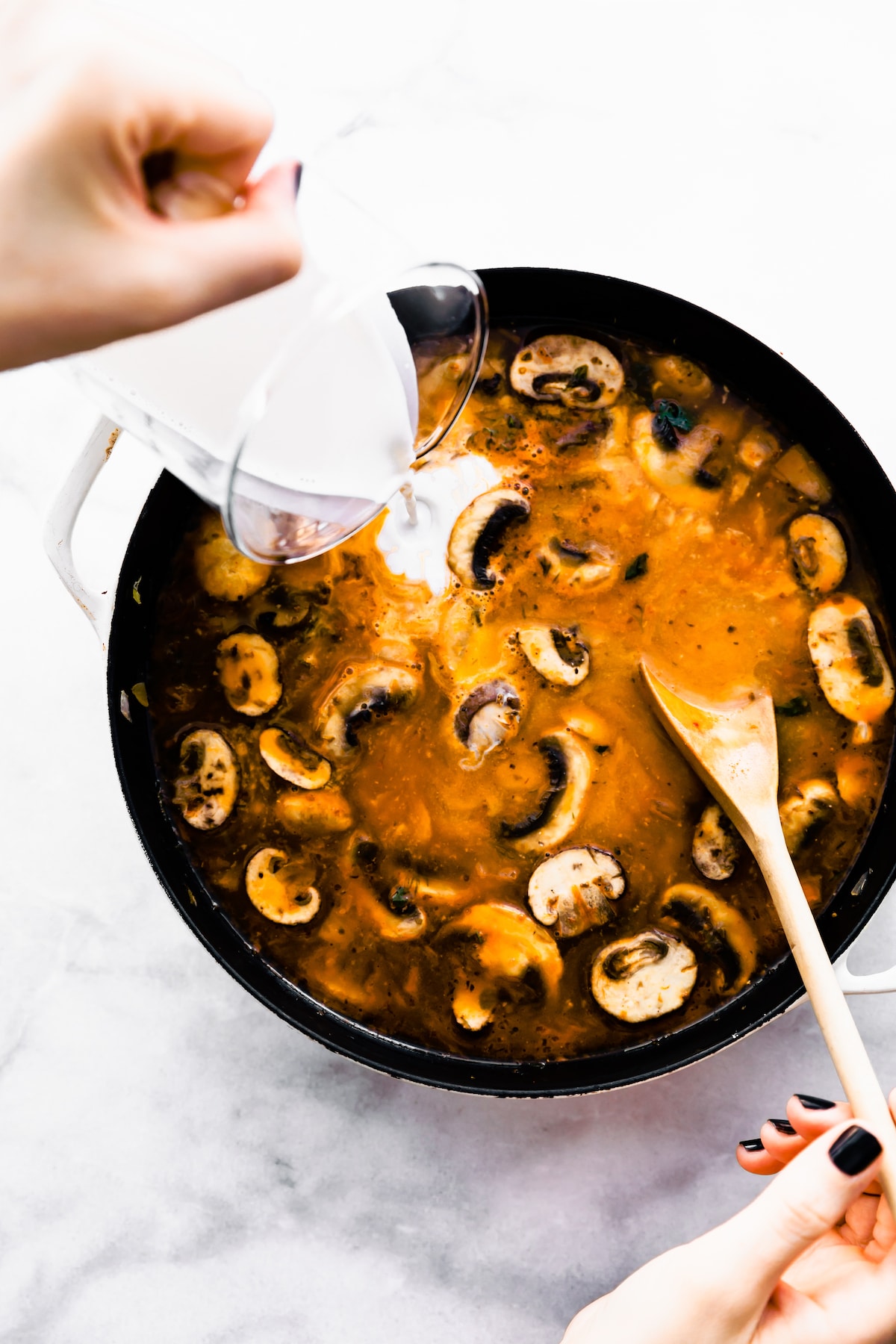 non-dairy milk being poured into a pot of mushroom soup with a wooden spoon sticking out