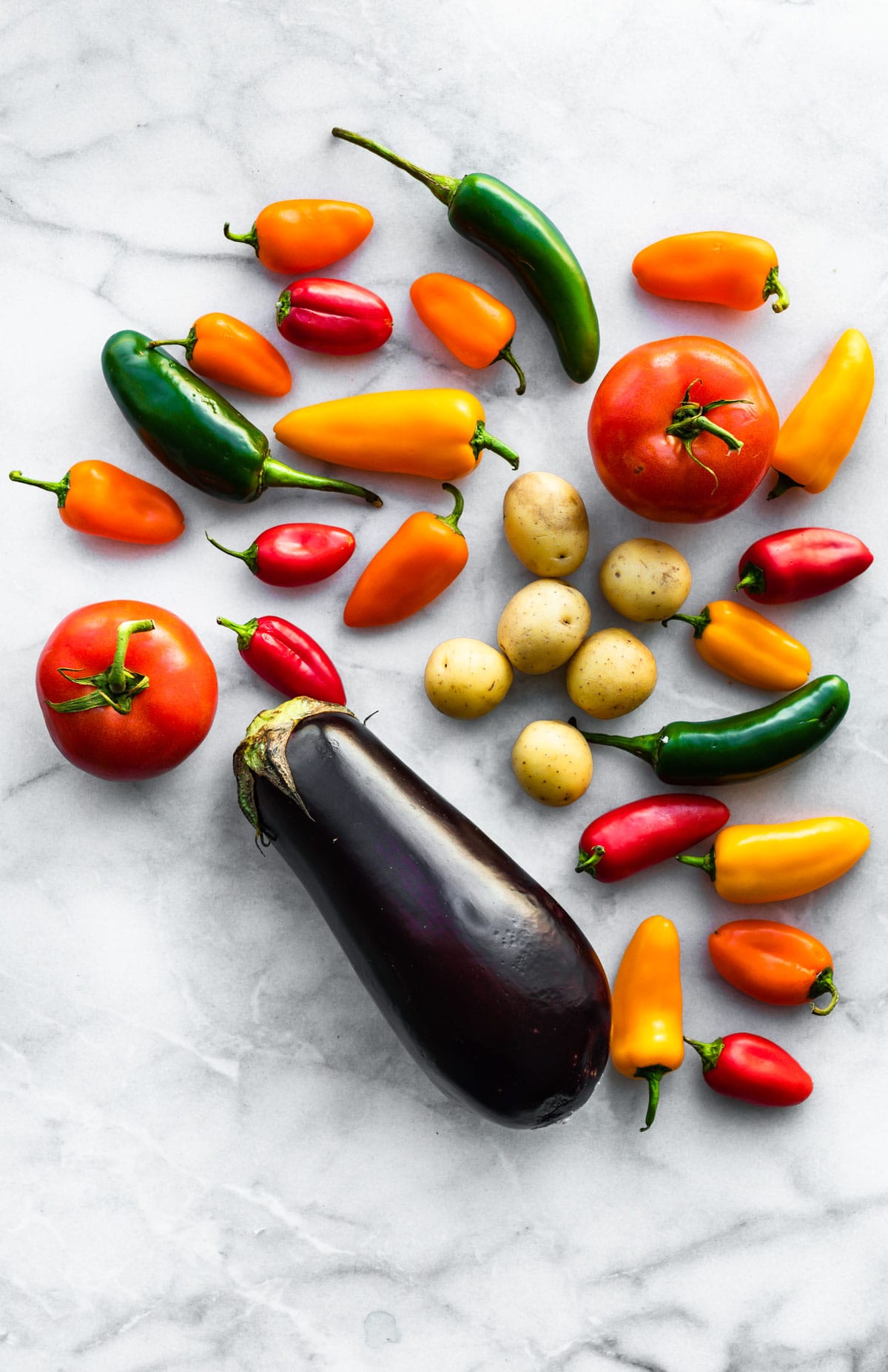 Nightshade vegetables like tomatoes, potatoes, jalapenos and colorful bell peppers on a grey countertop.