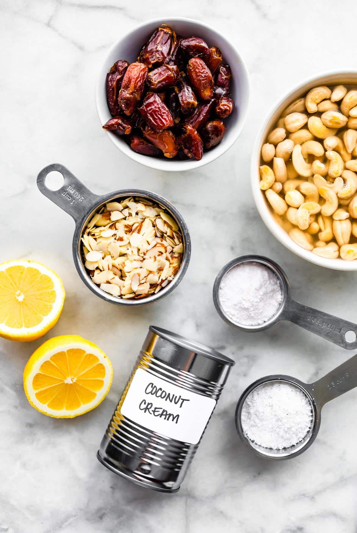 Cashews, dates, almonds, lemons, coconut cream, and protein powder all laid out separately.