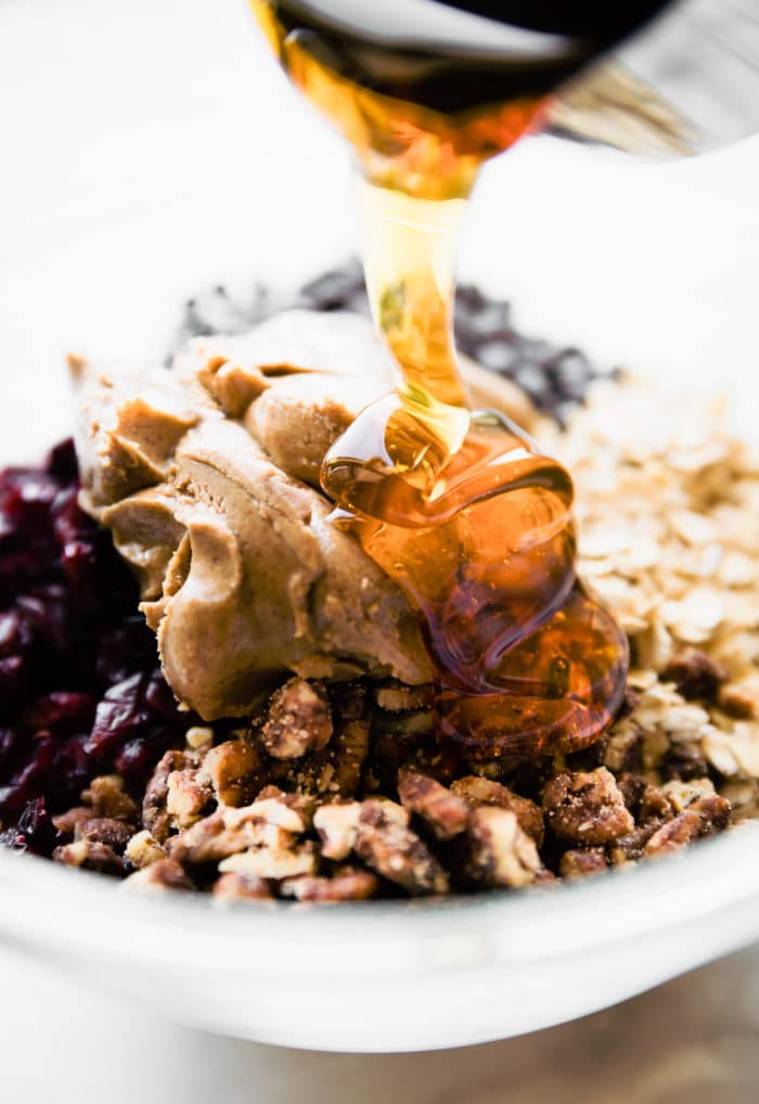 Close up view honey being poured into bowl filled with ingredients for no bake oatmeal energy balls.