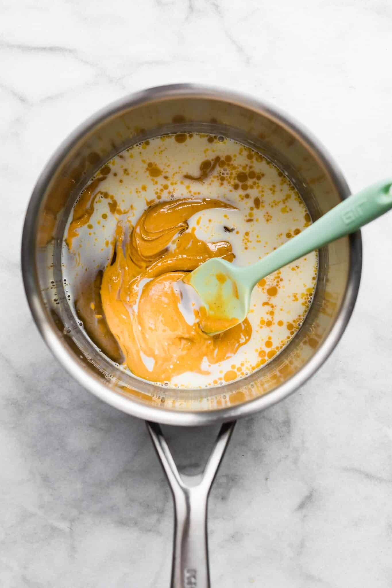 Peanut butter and milk mixed with a silicone spatula in a small soup pot.
