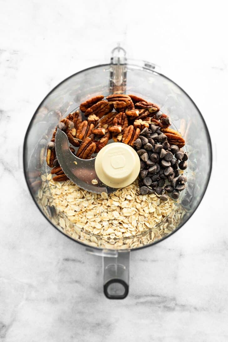 Food processor bowl filled with oats, pecans, and chocolate chips before blending