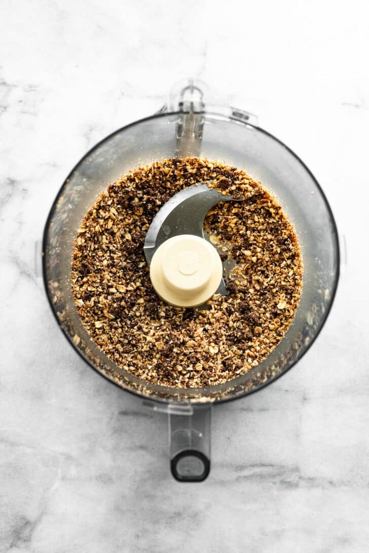 Blended pecans, oats, and chocolate chips in a food processor, showing a coarse crumb texture