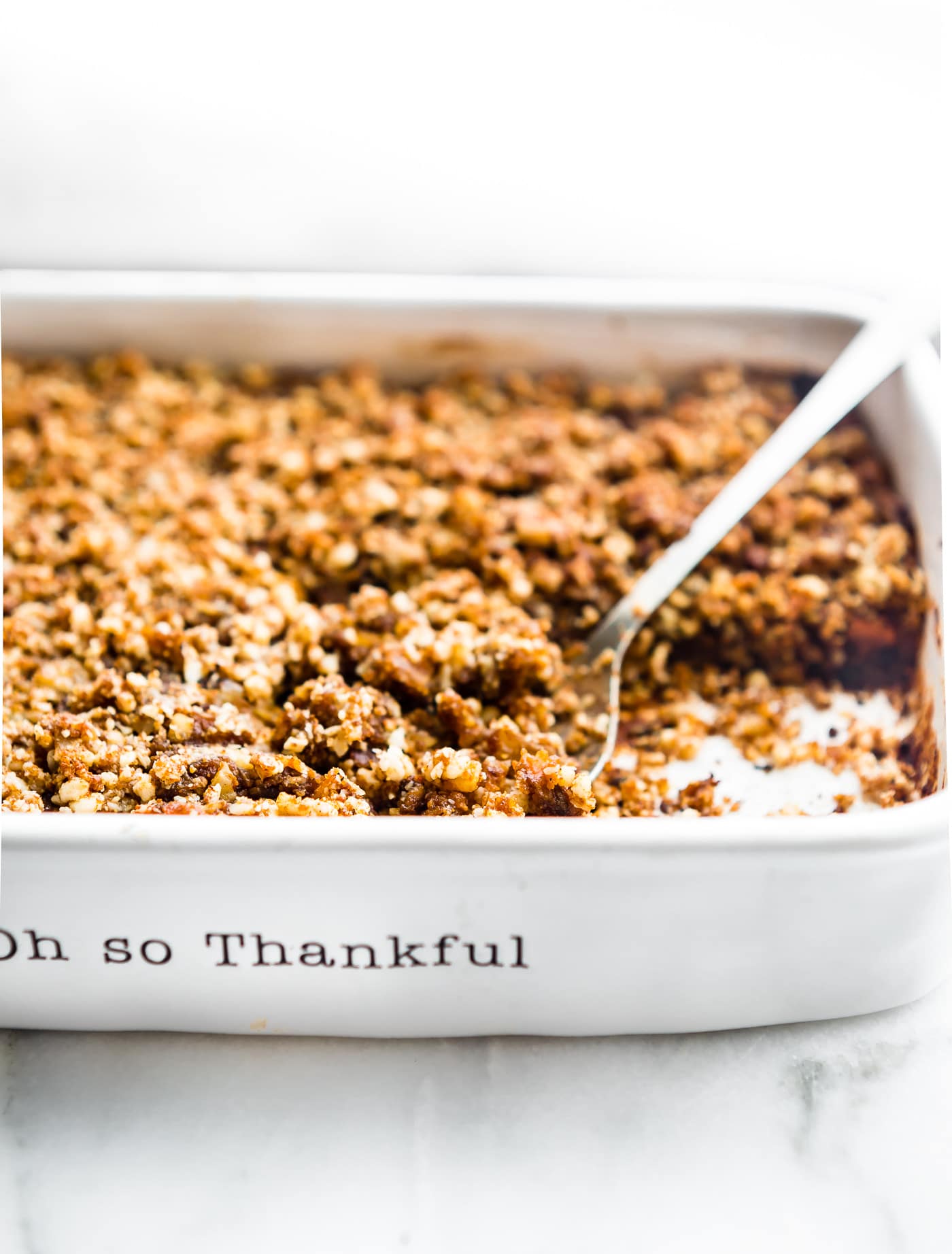Vegan sweet potato casserole with crumble topping in a white dish with serving spoon in it