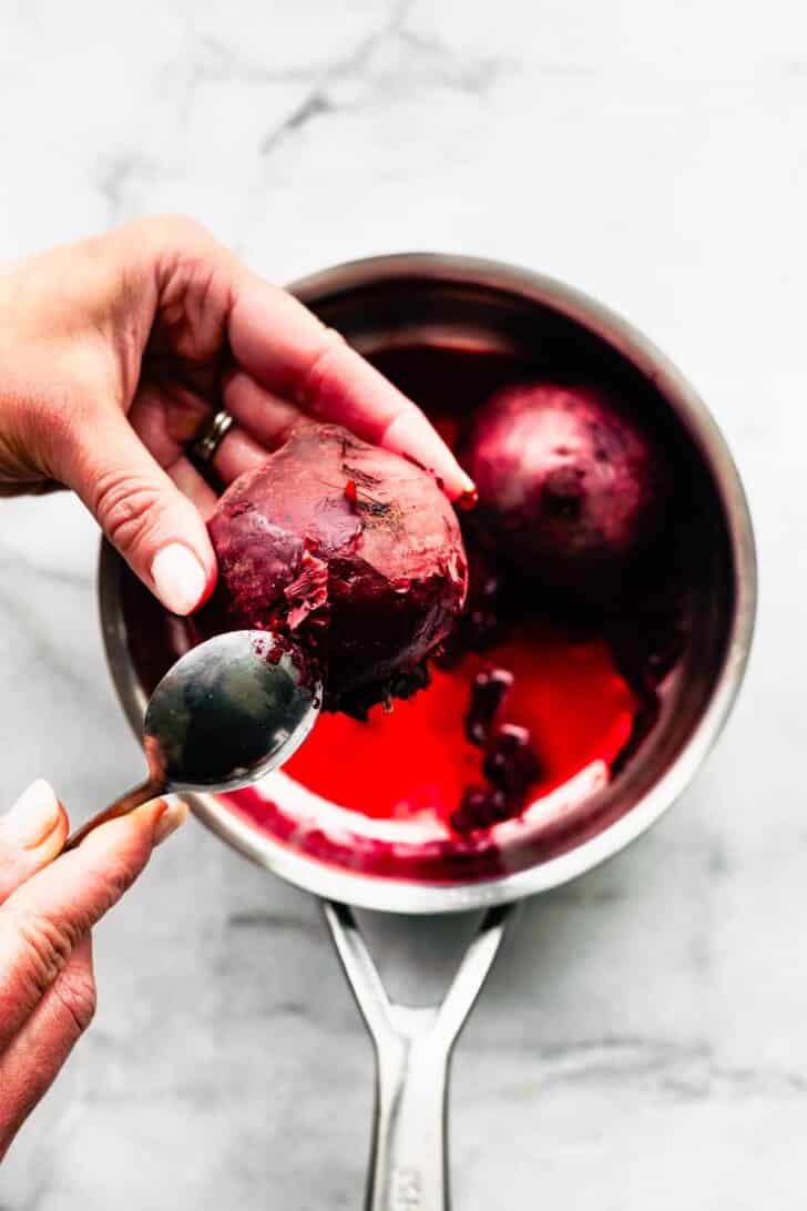 woman's hands holding and peeling steamed beets with a spoon