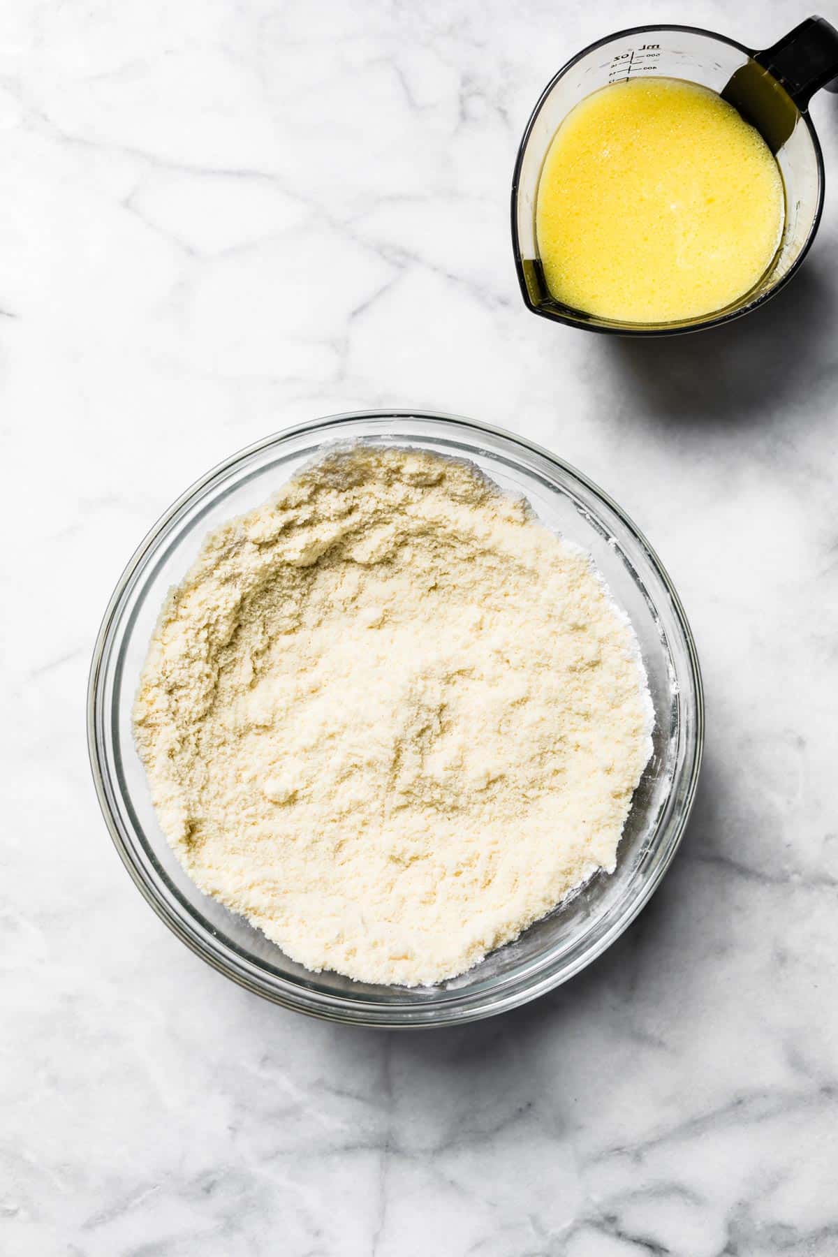 A bowl of almond flour and a measuring cup with whisked egg and milk.