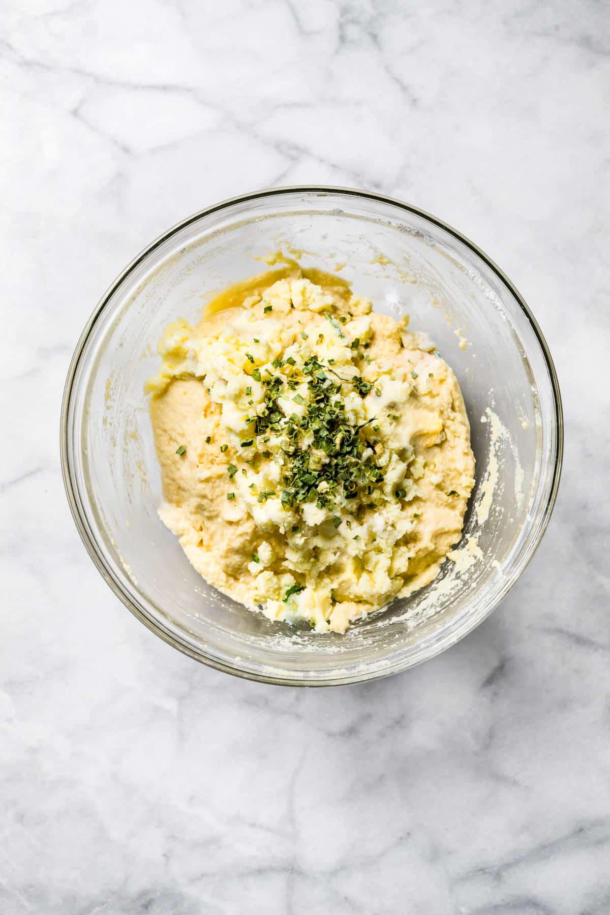 Fresh herbs sprinkled on gluten free potato bread batter in a glass bowl.