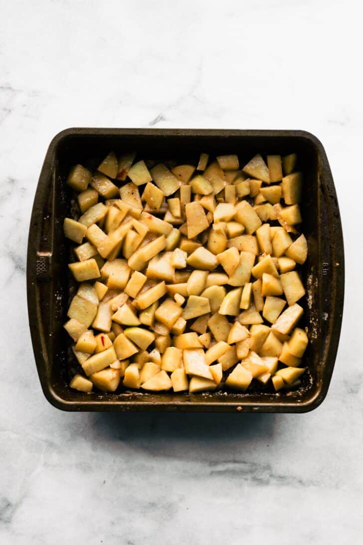 Chopped apples tossed with cinnamon and sugar in baking pan for filling layer.