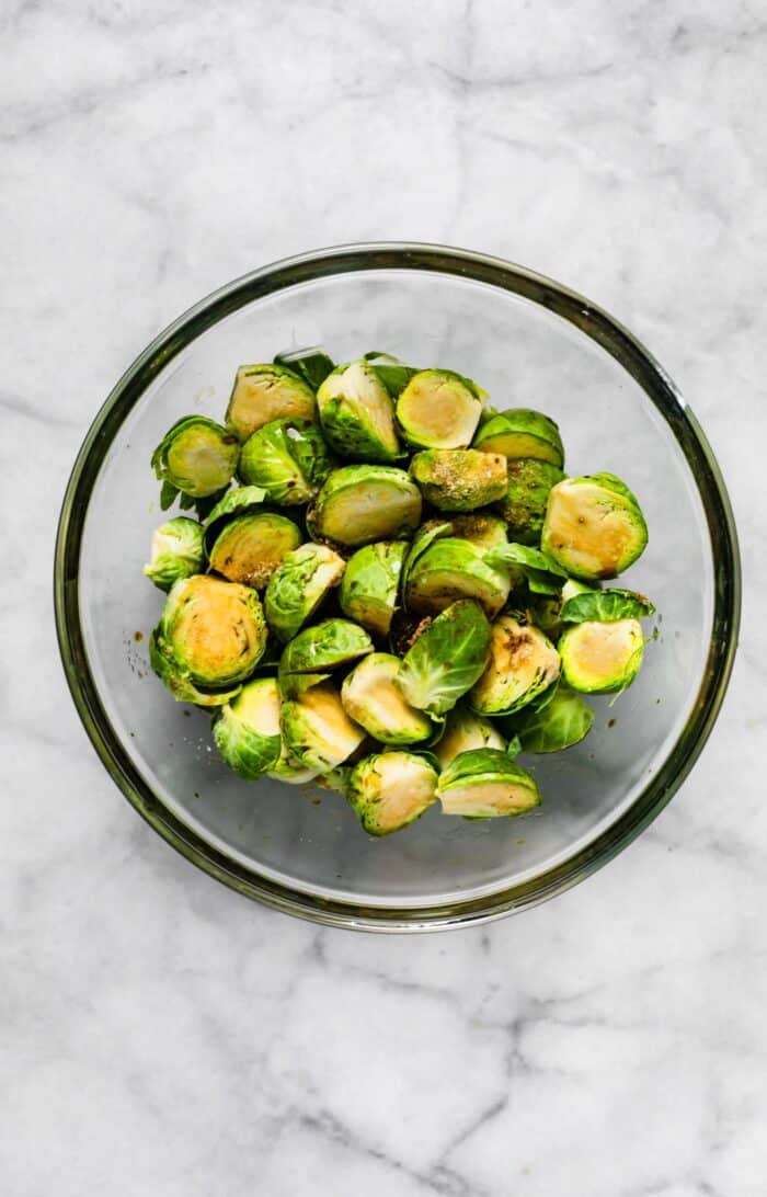 Halved Brussels sprouts tossed with oil and balsamic in a glass bowl.