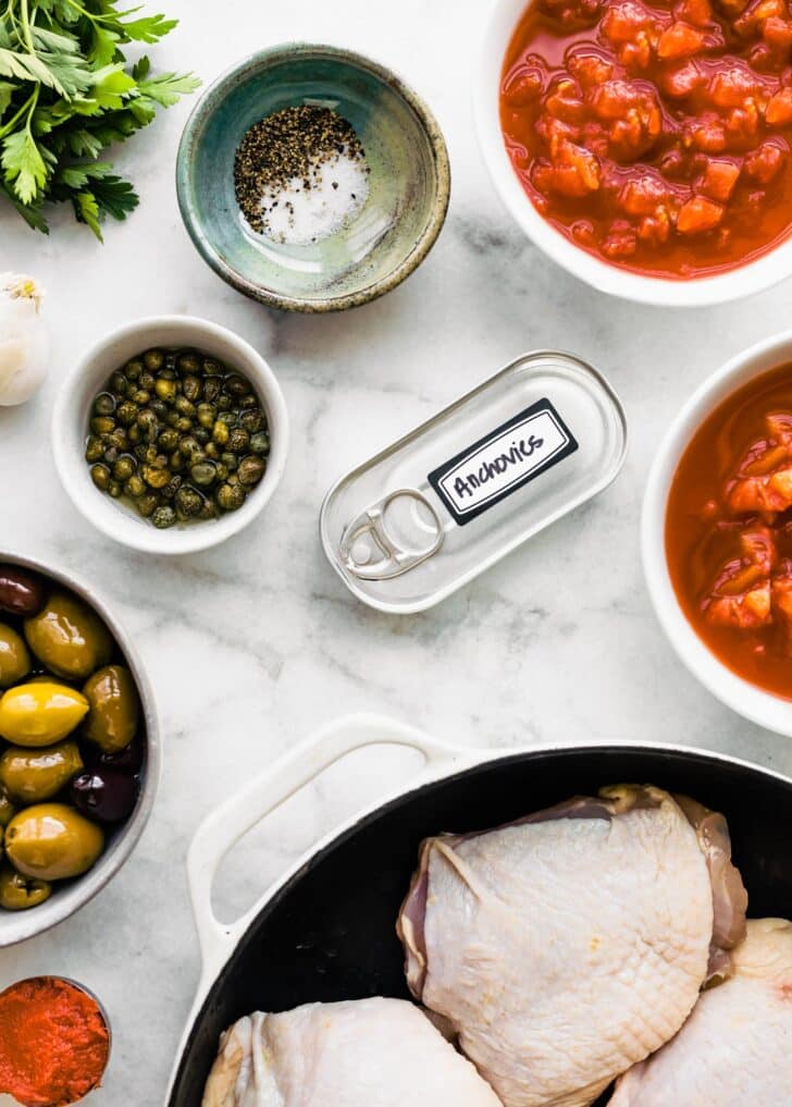 Ingredients for chicken puttanesca on a white marble countertop.