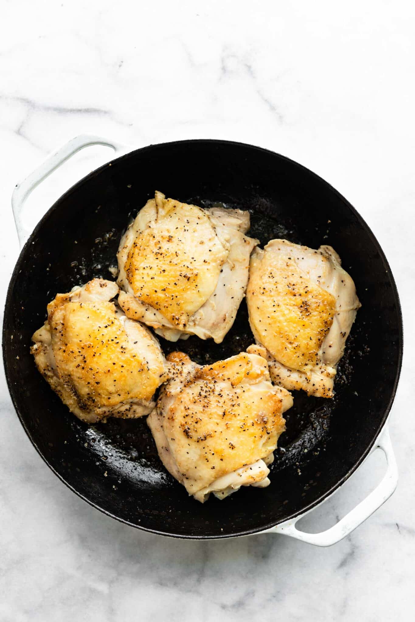 Browned skin on chicken thighs seasoned with salt and pepper in a cast iron skillet.