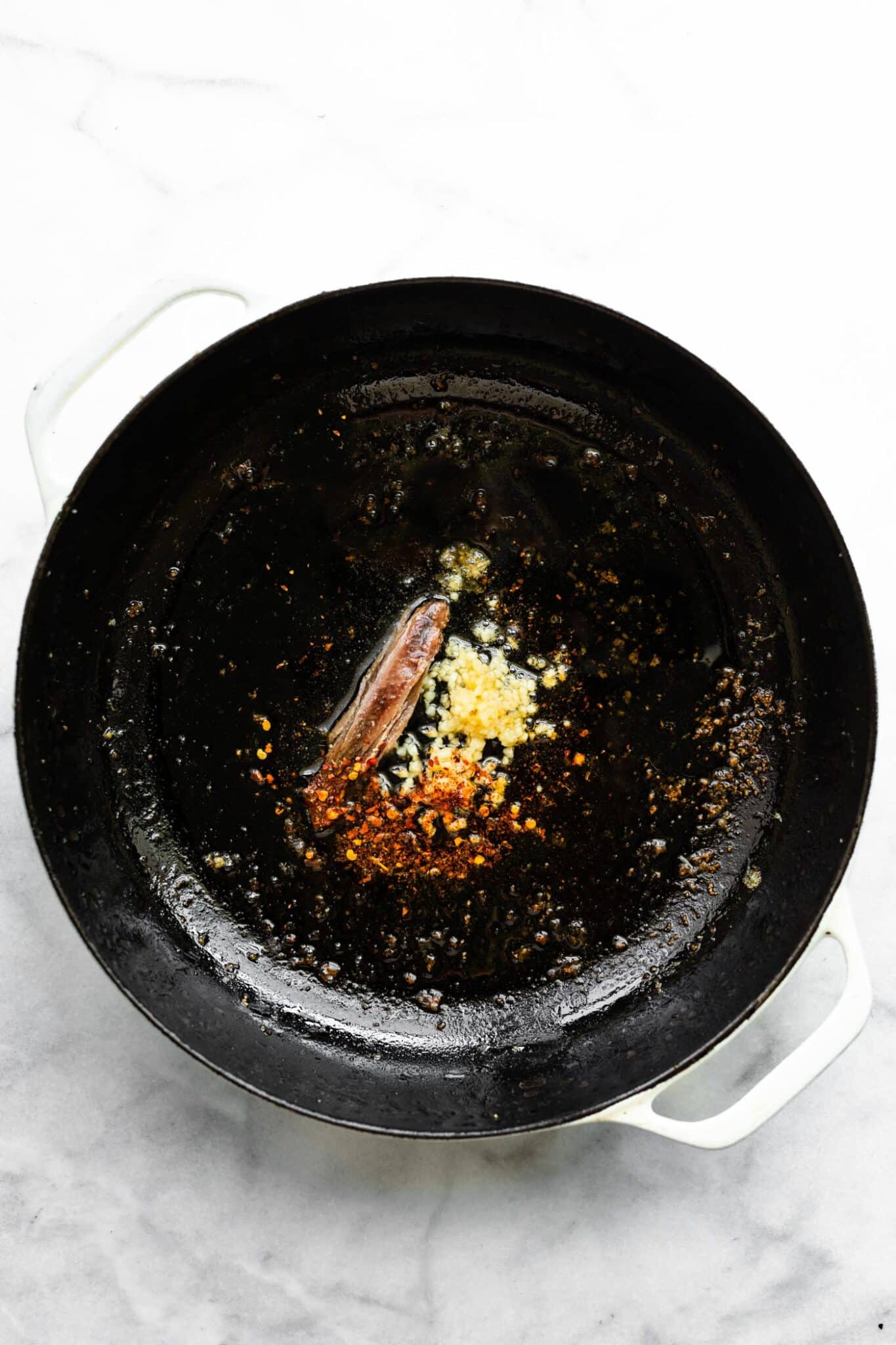An anchovy, garlic and red pepper flakes in a cast iron pan.