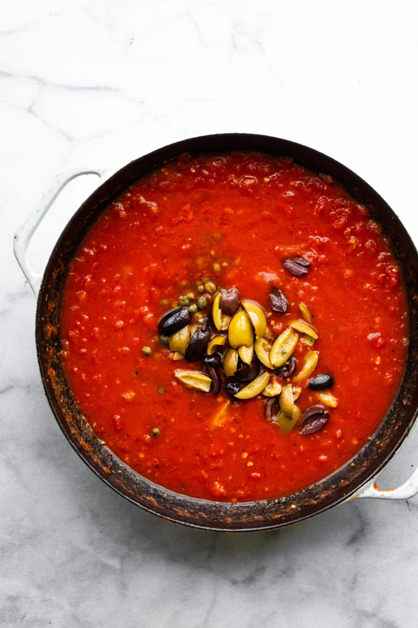Sliced olives placed on top of a tomato sauce mixture in a pan.