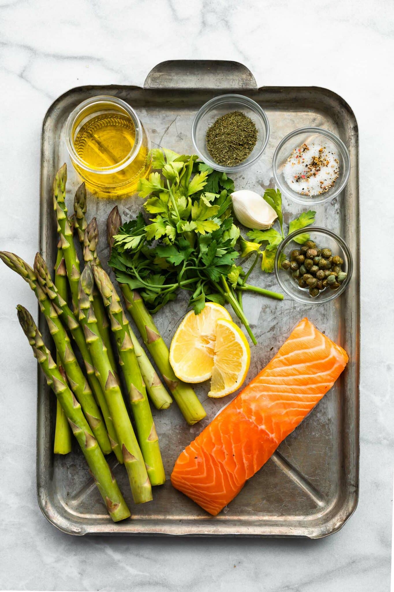 Ingredients for baked salmon and asparagus with herb sauce on a metal sheet pan.