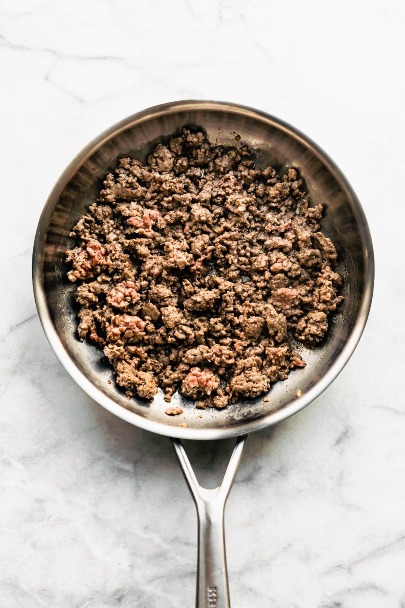A metal saute pan with browned ground beef.