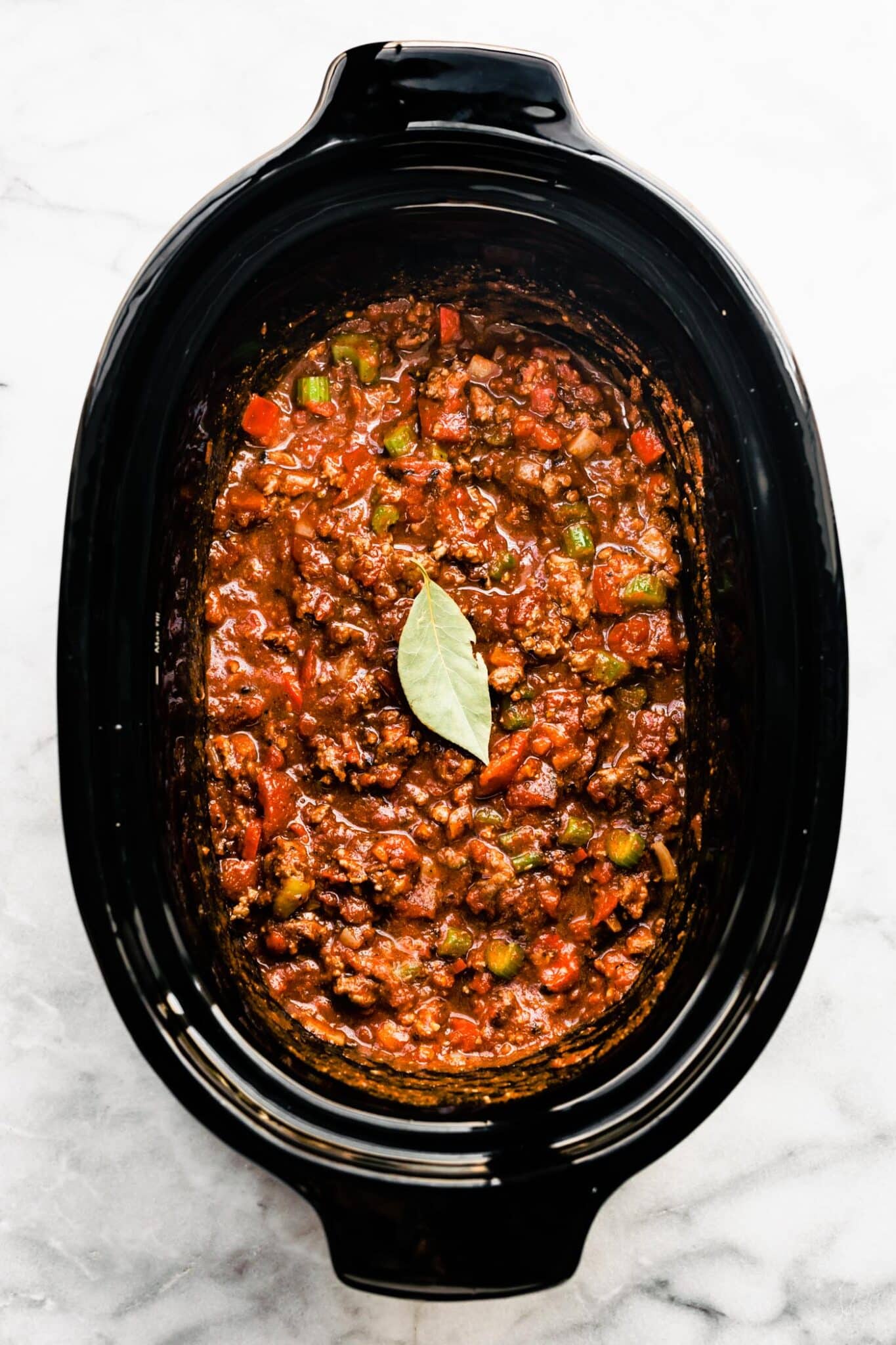 Overhead photo of a bay leaf atop a slow cooker with uncooked beef chili.